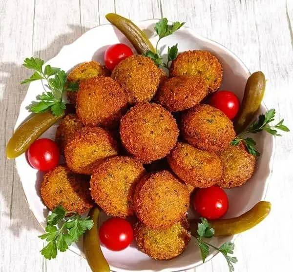 فلافل‌های خوشرنگ و لذیذ عمو حسین، طلایی و ترد، در بشقابی زیبا با گوجه‌گیلاسی‌های قرمز، جعفری تازه و خیارشور چیده شده‌اند.