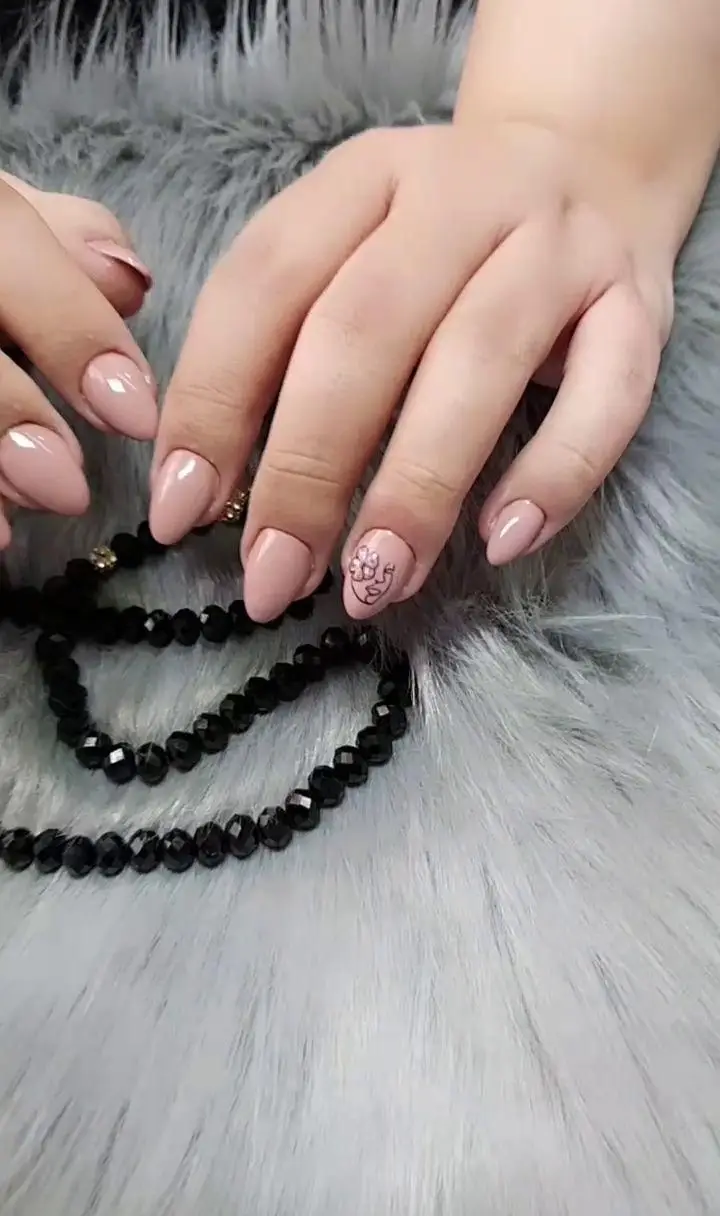 طراحی ناخن مینیمال با لاک نود و طرح صورت و گل روی ناخن بیضی شکل همراه با اکسسوری دستبند مشکی روی پس‌زمینه خز خاکستری