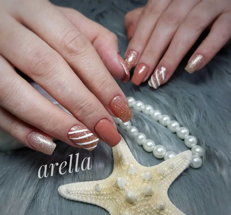 طراحی ناخن شیک با لاک گلبهی و اکلیلی طلایی به همراه خطوط مورب سفید، دیزاین ناخن تابستانی با ستاره دریایی و مروارید