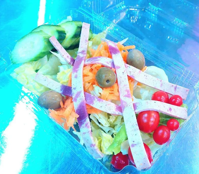 سالاد تازه و رنگارنگ فست فود آرام ناز با کاهو، هویج، خیار، زیتون، گوجه گیلاسی و کالباس در ظرف شفاف آماده سرو.