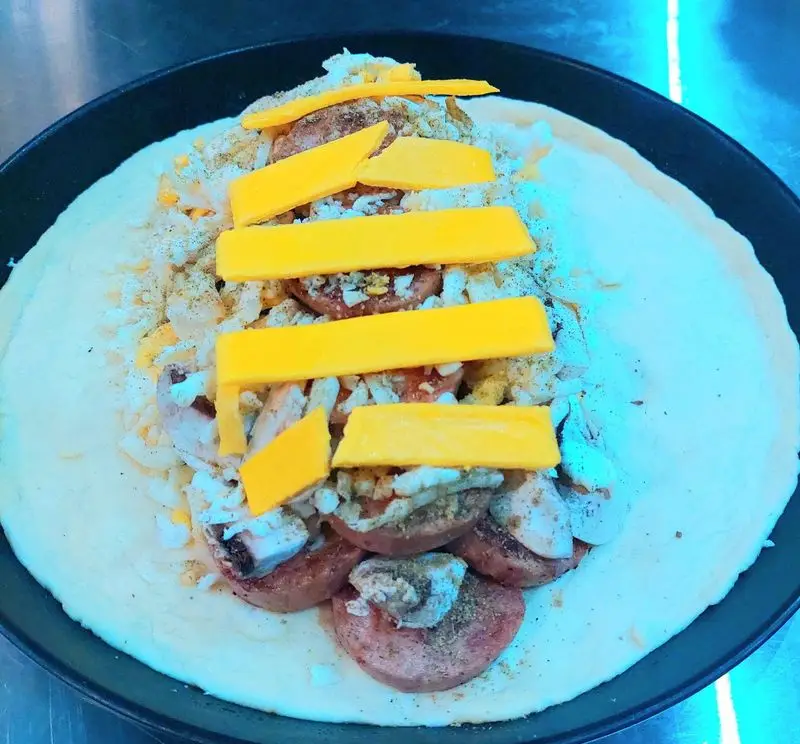 آماده سازی پیتزا با سوسیس، قارچ، پنیر چدار و مخلفات تازه در فست فود آرام ناز برای یک تجربه غذایی لذیذ و دلپذیر.