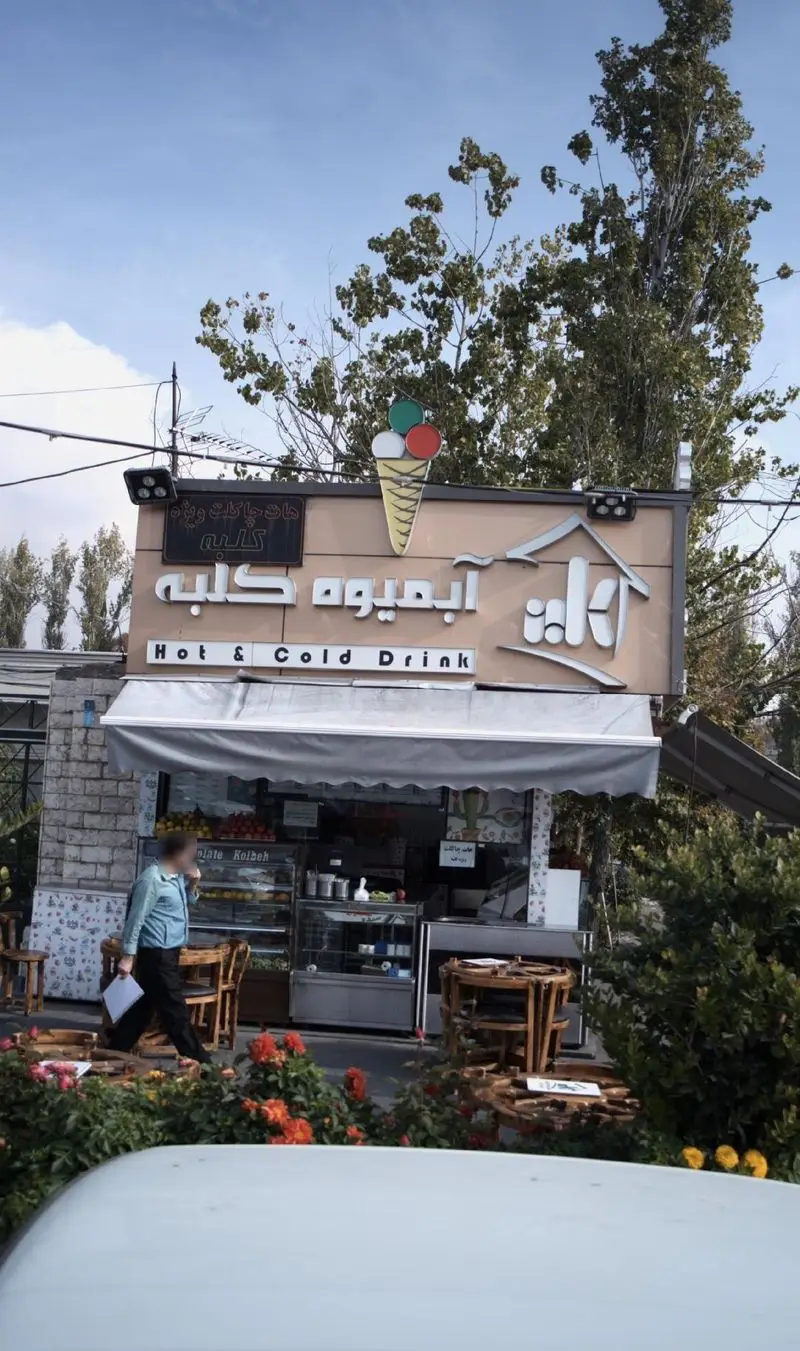 آبمیوه و بستنی ما ۲ تا (کلبه سابق) با تابلوی آبمیوه کلبه، لوگو بستنی و فضای روباز با میز و گل. مناسب نوشیدنی گرم و سرد.