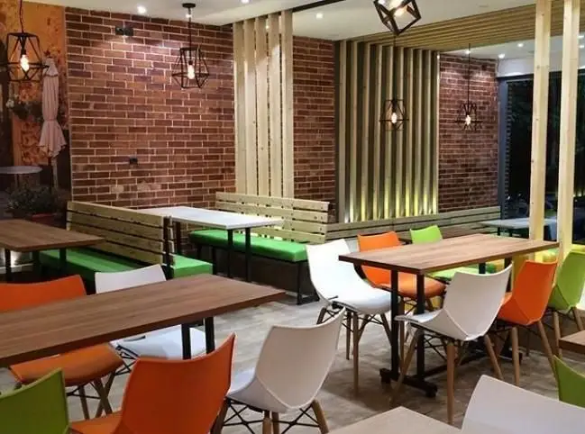 فضای داخلی دلنشین و مدرن پیتزایی پاروت با دیوار آجری، پارتیشن‌های چوبی، نیمکت‌های راحت سبز و میز و صندلی‌های رنگارنگ شیک.