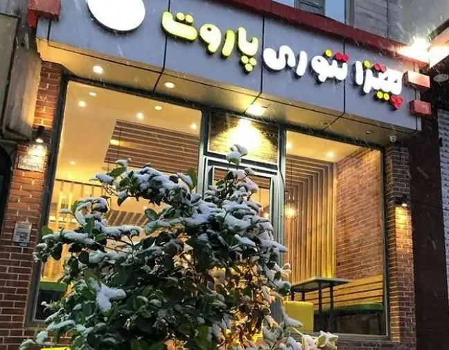 نمای بیرونی دنج پیتزایی پاروت در یک روز برفی زمستانی، با تابلو روشن و محیط داخلی گرم برای تجربه پیتزا و فست فود.