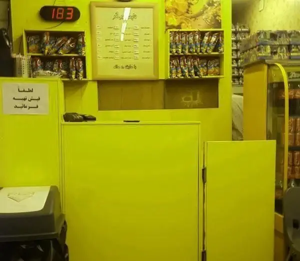 نمای داخلی پیشخوان فست فود برگر تاپس با دکوراسیون زرد، منوی غذا، نمایشگر نوبت ۱۸۳ و محصولات آماده سفارش مشتریان.