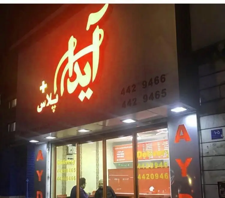 نمای بیرونی شبانه ساندویچ آیدا پلاس مرزداران با تابلوی نئونی درخشان، شماره‌های تماس 4429466 و 4429465 و فضای داخلی روشن