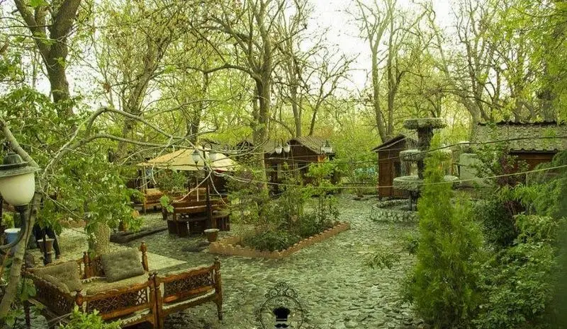 باغ رستوران شادی، فضای سبز و دلنشین با تخت‌های سنتی و آلاچیق‌های چوبی، محیطی طبیعی برای تجربه غذایی لذت‌بخش در فضای باز.