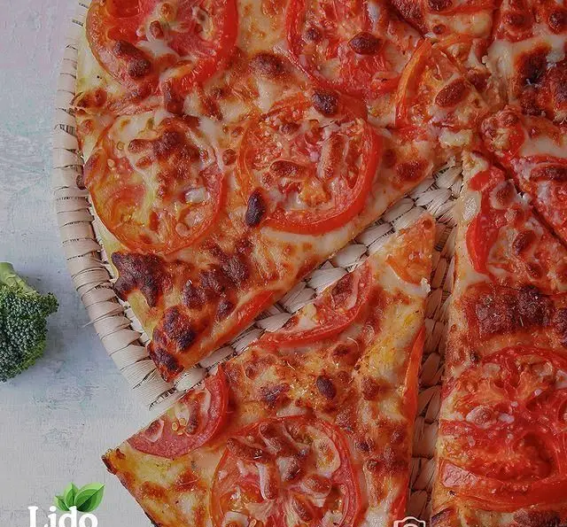 پیتزا گوجه و پنیر داغ و خوشمزه رستوران ایتالیایی لیدو، با برش‌های منظم و پنیر طلایی شده روی سینی حصیری.