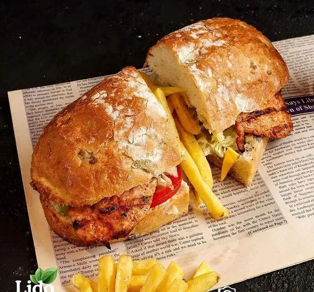 ساندویچ بزرگ و خوش طعم مرغ گریل رستوران ایتالیایی لیدو، با نان برشته، کاهو، گوجه فرنگی و سیب‌زمینی سرخ شده تازه. لذت یک غذای ایتالیایی.