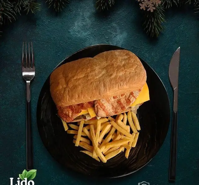 ساندویچ مرغ گریل شده با نان باگت و سیب‌زمینی سرخ کرده در بشقاب مشکی، از رستوران ایتالیایی لیدو، با تزئینات زمستانی.