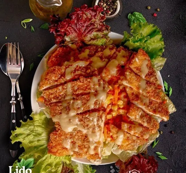 عکس هوایی از سالاد مرغ سوخاری ترد و سس‌دار رستوران ایتالیایی لیدو با کاهو، ذرت و هویج تازه برای ناهار یا شام.