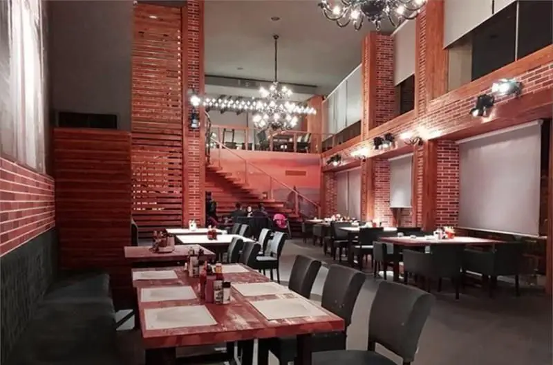 فضای داخلی جذاب و دلباز رستوران ایتالیایی لیدو با دکوراسیون مدرن آجری و چوبی، لوستر بزرگ و پلکانی به طبقه بالا. میز و صندلی های چیده شده آماده سرویس دهی به مشتریان.
