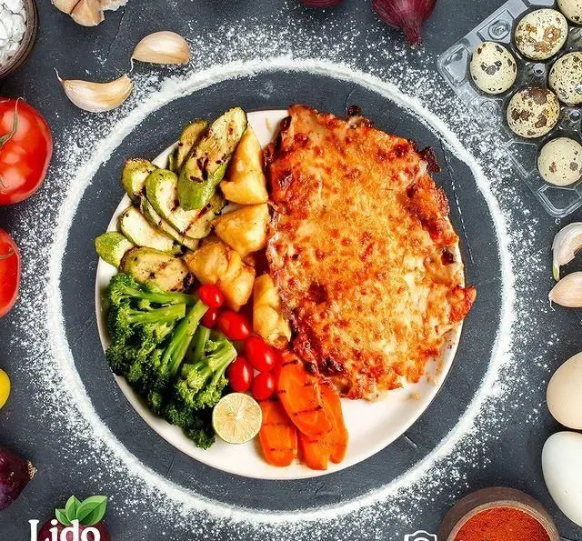 غذای ایتالیایی رستوران لیدو: مرغ پارمزان با سبزیجات تازه گریل شده (کدو، بروکلی، هویج). یک وعده سالم و لذیذ برای شام یا ناهار.