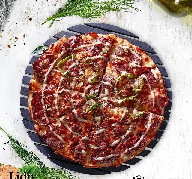 پیتزای خوشمزه و پرملات رستوران ایتالیایی لیدو با قارچ، فلفل دلمه و تکه‌های گوشت، تزئین شده با سس سفید مخصوص.
