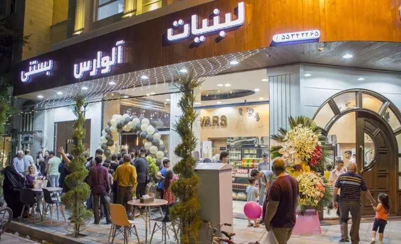 نمای شلوغ فروشگاه لبنیات بستنی آلوارس در شب، با حضور مشتریان، تزئینات افتتاحیه، ارائه محصولات لبنی و بستنی