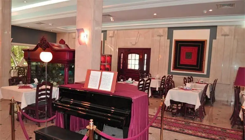 نمای داخلی رستوران ایرانی استخر ونک با دکوراسیون کلاسیک، میزهای چیده شده و پیانوی مشکی در مرکز. محیطی دلنشین و مجلل برای غذاخوری.