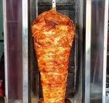 شاورما خالو: یک رول بزرگ و خوشرنگ گوشت شاورما روی سیخ گردان، آماده برای برش و تهیه ساندویچ‌های لذیذ و محبوب.