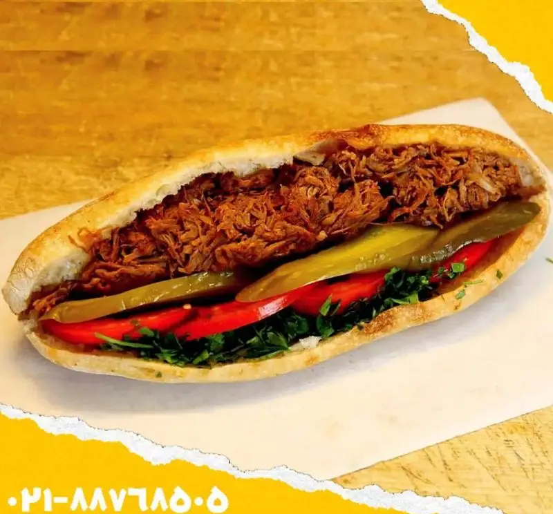 ساندویچ مخصوص و خوشمزه اغذیه یگانه با نان باگت، گوشت ریش‌ریش، گوجه فرنگی، خیارشور و جعفری تازه؛ غذایی لذیذ و پرطرفدار.