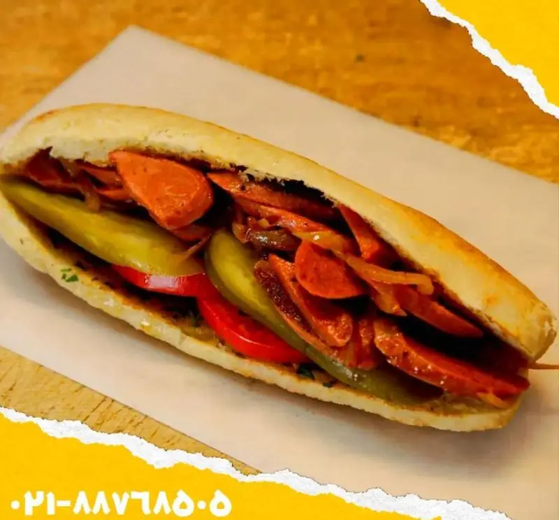 تصویری جذاب از یک ساندویچ سوسیس و کالباس تازه و لذیذ اغذیه یگانه، پر شده با خیارشور و گوجه فرنگی، انتخابی عالی برای فست فود.