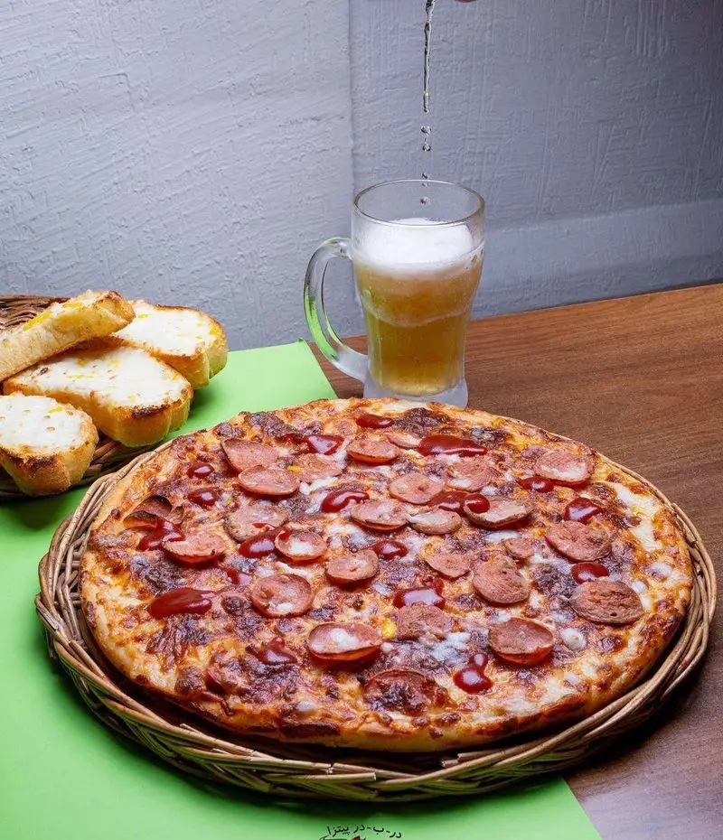 پیتزای سوسیس و کالباس داغ و خوشمزه از پیتزا درب در، همراه با نان سیر و نوشیدنی خنک، ایده‌آل برای یک وعده لذت‌بخش.