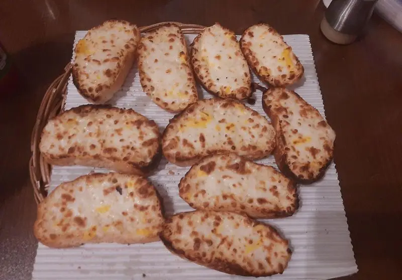 نان سیر پنیری با پنیر ذوب شده و برشته طلایی، آماده سرو در پیتزا در ب در، انتخابی عالی برای شروع یک وعده غذایی.