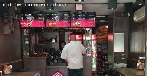 نمایی داخلی از خانه پیتزا با مردی در لباس آشپز پشت کانتر، منوهای دیجیتال روشن و فضایی مدرن و تمیز برای سفارش غذاهای فست فود.