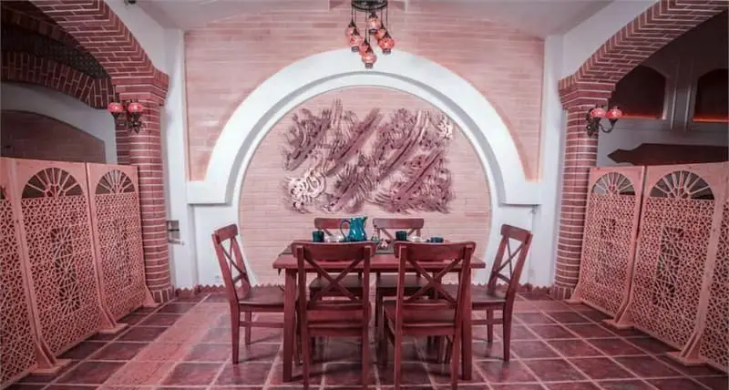 نمایی از دکوراسیون داخلی رستوران مسینه، با آجرکاری هنرمندانه، طاق‌نمای چشمگیر، میز غذاخوری چوبی و پنل‌های مشبک با طرح سنتی.