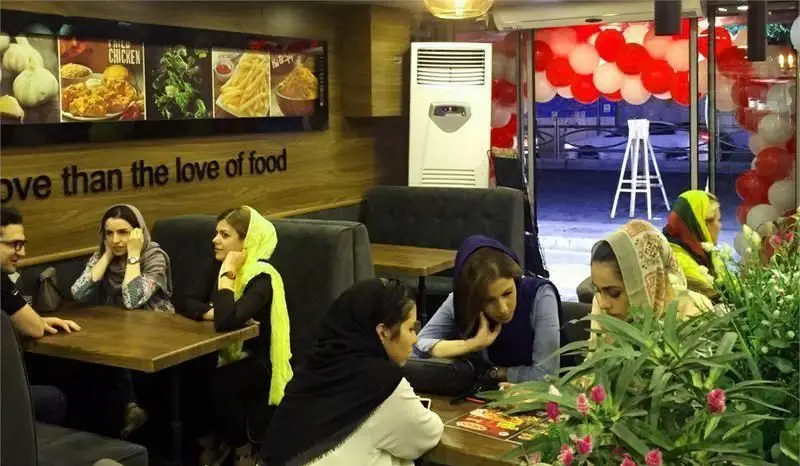 فضای داخلی فست فود آمادو مملو از مشتریان، با منوی متنوع از غذاهای خوشمزه و دکوراسیون جذاب شامل بادکنک‌های قرمز و سفید.