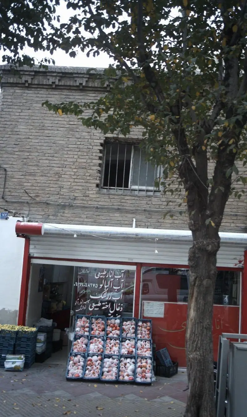 مغازه آب انار طبیعی و آبمیوه فروشی در خیابان، نمایش میوه‌های تازه فصلی از جمله انار و سایر میوه‌ها در جعبه‌های چیده شده، آماده برای آبگیری.