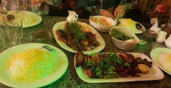 نمایی از میز پر از غذای ایرانی در کافه قلیان آقا بزرگ، شامل چلوکباب‌های لذیذ جوجه، کوبیده و برگ، همراه با برنج زعفرانی و مخلفات.
