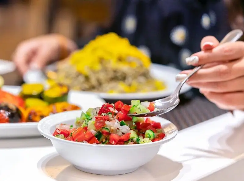نمایی نزدیک از سالاد شیرازی تازه و خوشرنگ شامل گوجه، خیار و پیاز در رستوران محسن، آماده سرو کنار چلوکباب اصیل ایرانی.