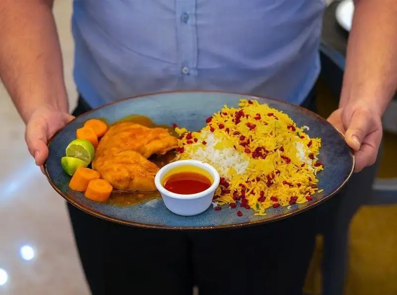 نمایی از چلو مرغ زرشک پلو با تزیین هویج و لیمو، یک غذای سنتی ایرانی از منوی متنوع و خوشمزه رستوران محسن. لذت طعم واقعی.