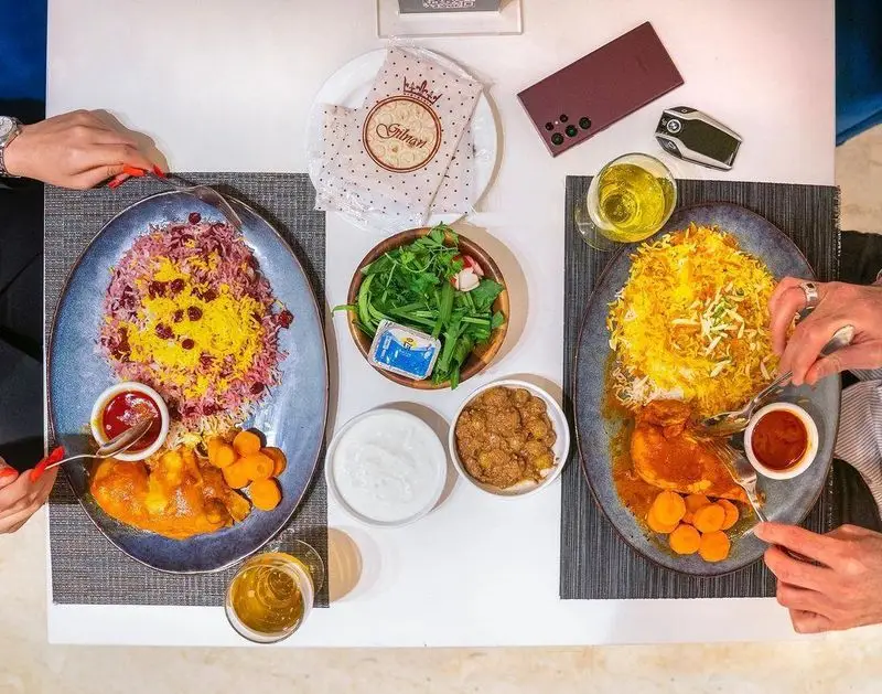 میز غذای کامل و دلپذیر در رستوران محسن: دو بشقاب برنج ایرانی با ته دیگ زعفرانی و زرشک، خورشت مرغ و مخلفات تازه.