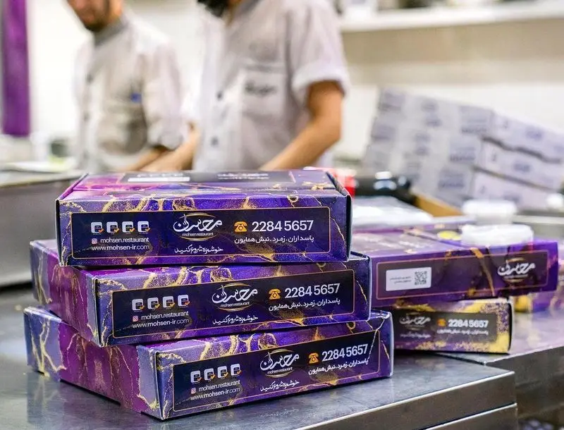 بسته‌بندی‌های شیک و مدرن رستوران محسن با طرح بنفش و طلایی در آشپزخانه، شامل آدرس پاسداران و شماره تماس 22845657.