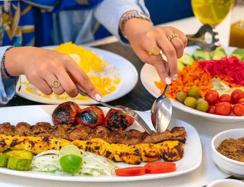 مشتری در حال سرو چلوکباب کوبیده و جوجه به همراه گوجه، برنج و سالاد در رستوران محسن. غذای لذیذ ایرانی.
