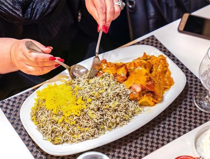 مشتری در حال سرو غذای باقالی پلو و برنج زعفرانی همراه با خورش گوشت لذیذ در رستوران محسن. تجربه‌ای لذت‌بخش از غذای ایرانی.