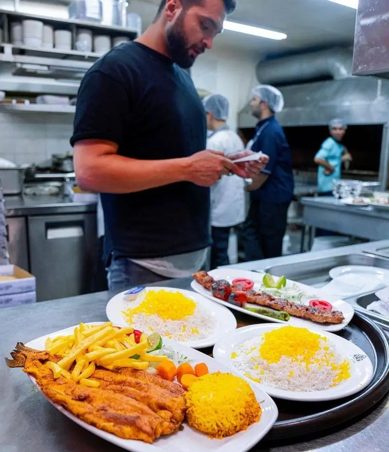 نمای داخلی آشپزخانه رستوران محسن: سرآشپز در حال آماده سازی کباب و ماهی تازه در کنار چلو زعفرانی. طعم اصیل غذای ایرانی.