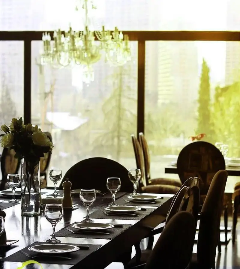 فضای داخلی شیک و لوکس رستوران فرنگی وی آی پی سورینت با میز غذاخوری چوبی مجلل، چیدمان کامل و لیوان‌های کریستال، همراه با چشم‌انداز شهری آرامش‌بخش.