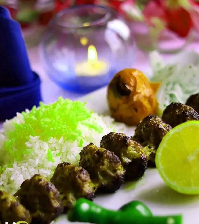 نمای نزدیک از کباب و برنج سفید با سبزیجات و لیموی تازه، در کنار شمع روشن، از منوی لذیذ رستوران فرنگی وی آی پی سورینت.