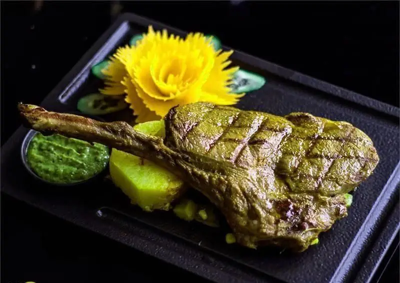 نمای نزدیک از دنده گوسفندی کبابی با سس سبز و سیب زمینی، تزئین شده با گل زیبا در رستوران فرنگی وی آی پی سورینت.