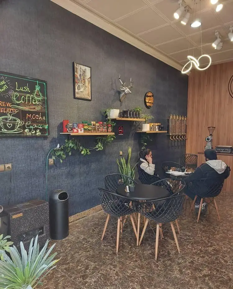 فضای داخلی دنج و مدرن کافه قهوه لوش، با مشتریانی در حال لذت بردن از نوشیدنی‌ها، دکوراسیون شیک و منوی متنوع قهوه.