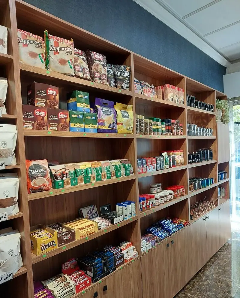 قفسه‌های چوبی قهوه لوش پر از انواع قهوه، کاپوچینو، نسکافه، شکلات‌های خارجی و تنقلات متنوع در یک فروشگاه مدرن.