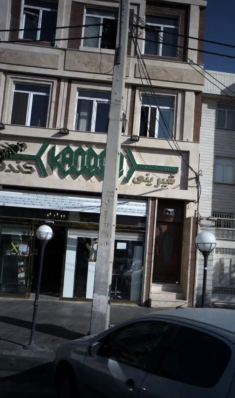 نمای بیرونی شیرینی کندو، قنادی محبوب در شهر، با تابلوی سبز رنگ برجسته، ورودی اصلی فروشگاه و پنجره های شیک.