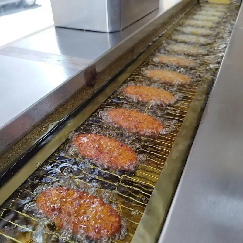 تصویری از فرآیند پخت شامی‌های خوشمزه و تازه در خط تولید پیشرفته غذای خانگی شامی یامی، سرخ شدن در روغن داغ.