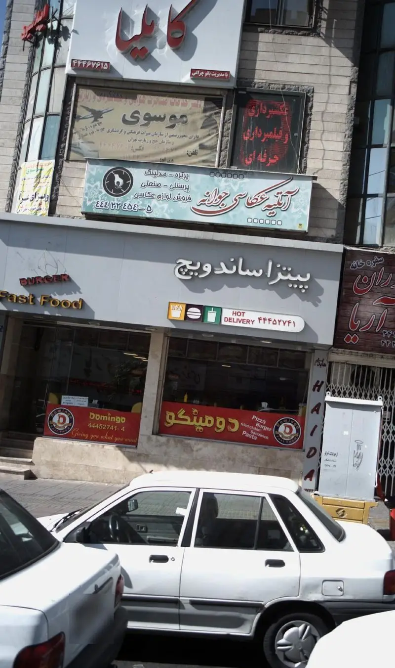 تصویر نمای بیرونی کسب و کار پیتزا ساندویچ و فست فود دومینگو با تابلوهای فارسی، ارائه دهنده پیتزا، برگر، ساندویچ و دلیوری.