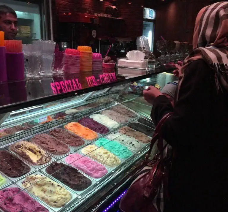 مشتری در حال انتخاب طعم‌های رنگارنگ و لذیذ بستنی از ویترین جذاب آبمیوه بستنی شاهو، برای تجربه‌ای دلنشین و شیرین.