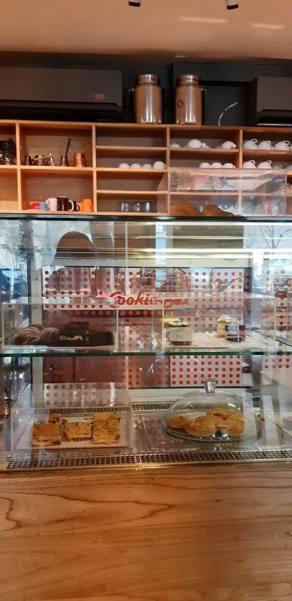 ویترین جذاب کوکی باکس در رستوران سبوس: نمایش دسرهای تازه، کوکی، کروسان و شیرینی. قفسه‌های چوبی با ظروف شیک قهوه.