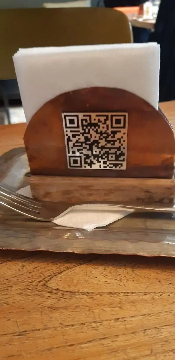 میز رستوران سبوس با نگهدارنده چوبی دستمال، کد QR منوی دیجیتال، قاشق و چنگال روی سینی فلزی برای تجربه سفارش آسان.