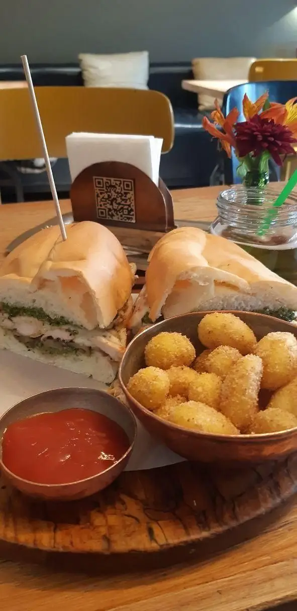 ساندویچ مرغ و سس سبز، کروکت سیب زمینی ترد و سس کچاپ روی میز چوبی در رستوران سبوس، تجربه‌ای خوشمزه از غذا.