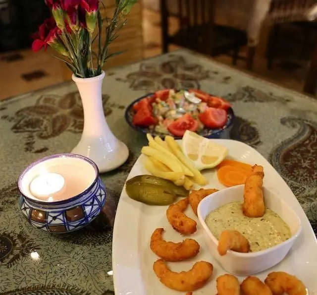 میگو سوخاری، سیب زمینی و سالاد در سفره خانه سنتی باغ فردوس؛ فضایی دلنشین با شمع و گل برای تجربه غذایی لذت‌بخش.